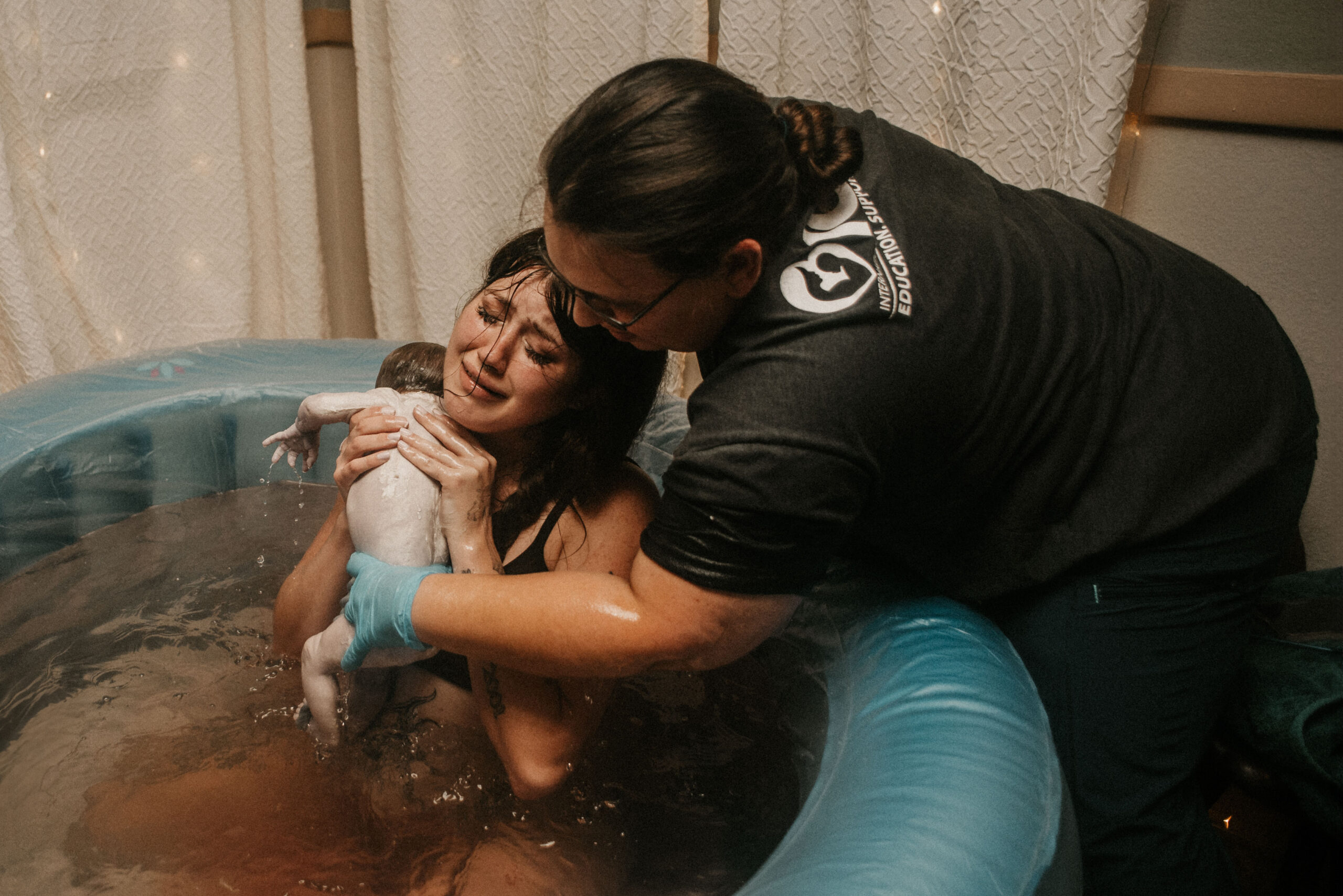Mother holding newborn in birth pool moments after delivery at A Mother’s Village Birth Center of Ocala, supported by a midwife.